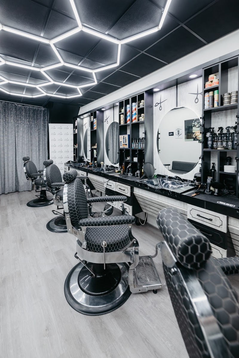 De salon: een rij chromen barbierstoelen met zwarte bekleding, ronde spiegels en hexagonverlichting aan het plafond.